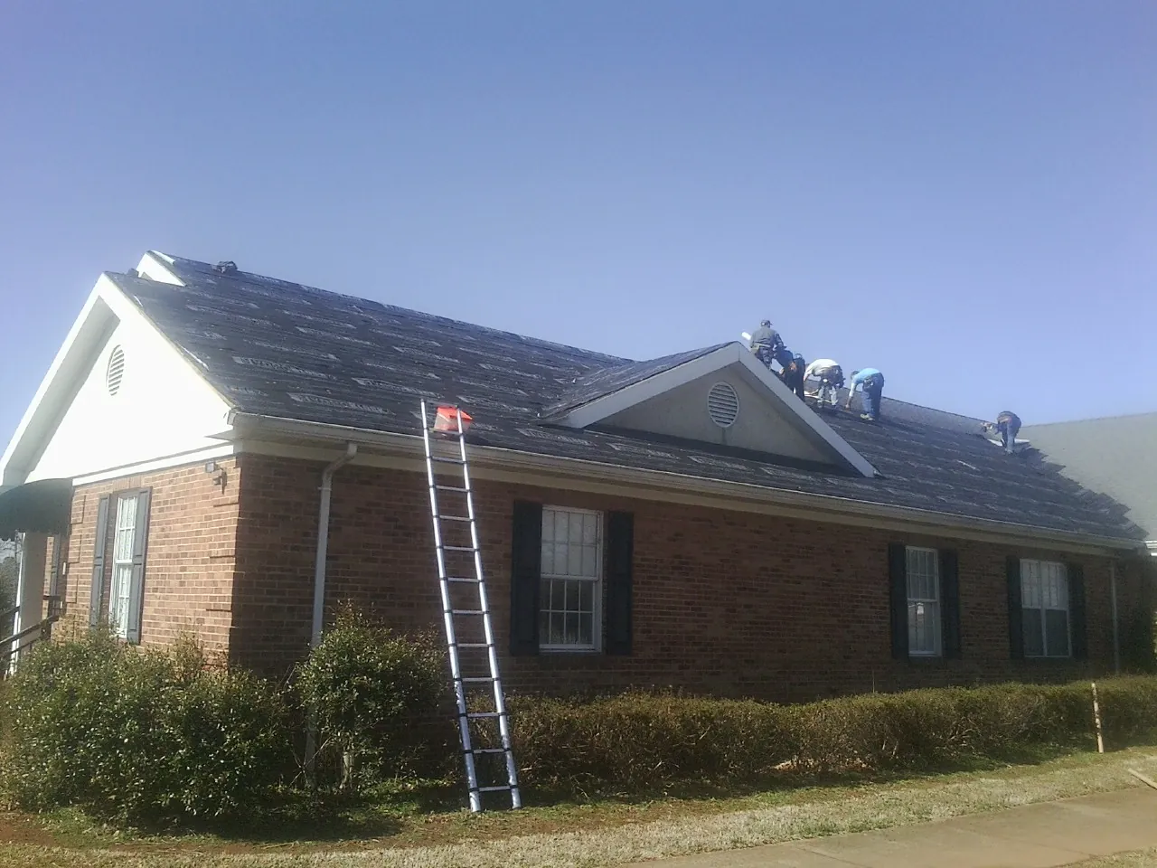 Crew tearing shingles off a brick ranch roof with a ladder set — Metal Roof Repair work by our crew in Lyman