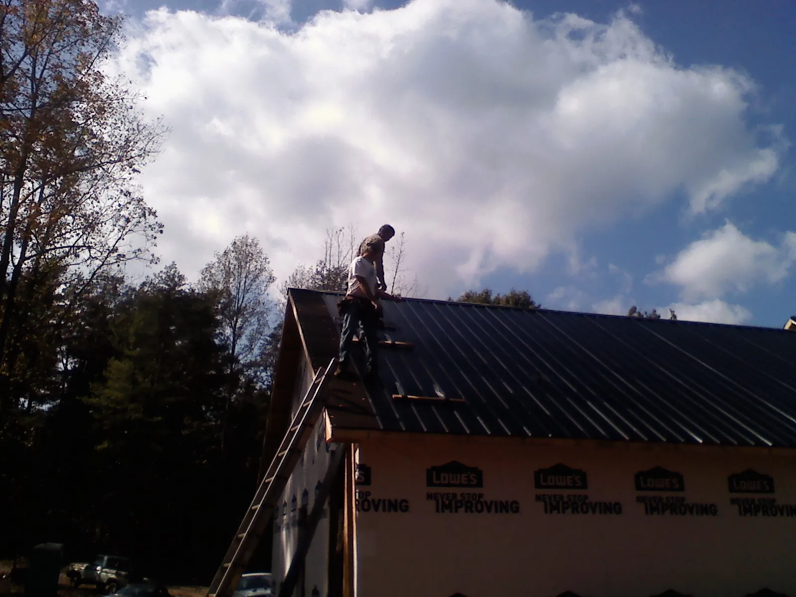 Roofer fastening dark metal panels high against a cloudy sky, from a Roof Inspection job in Lyman